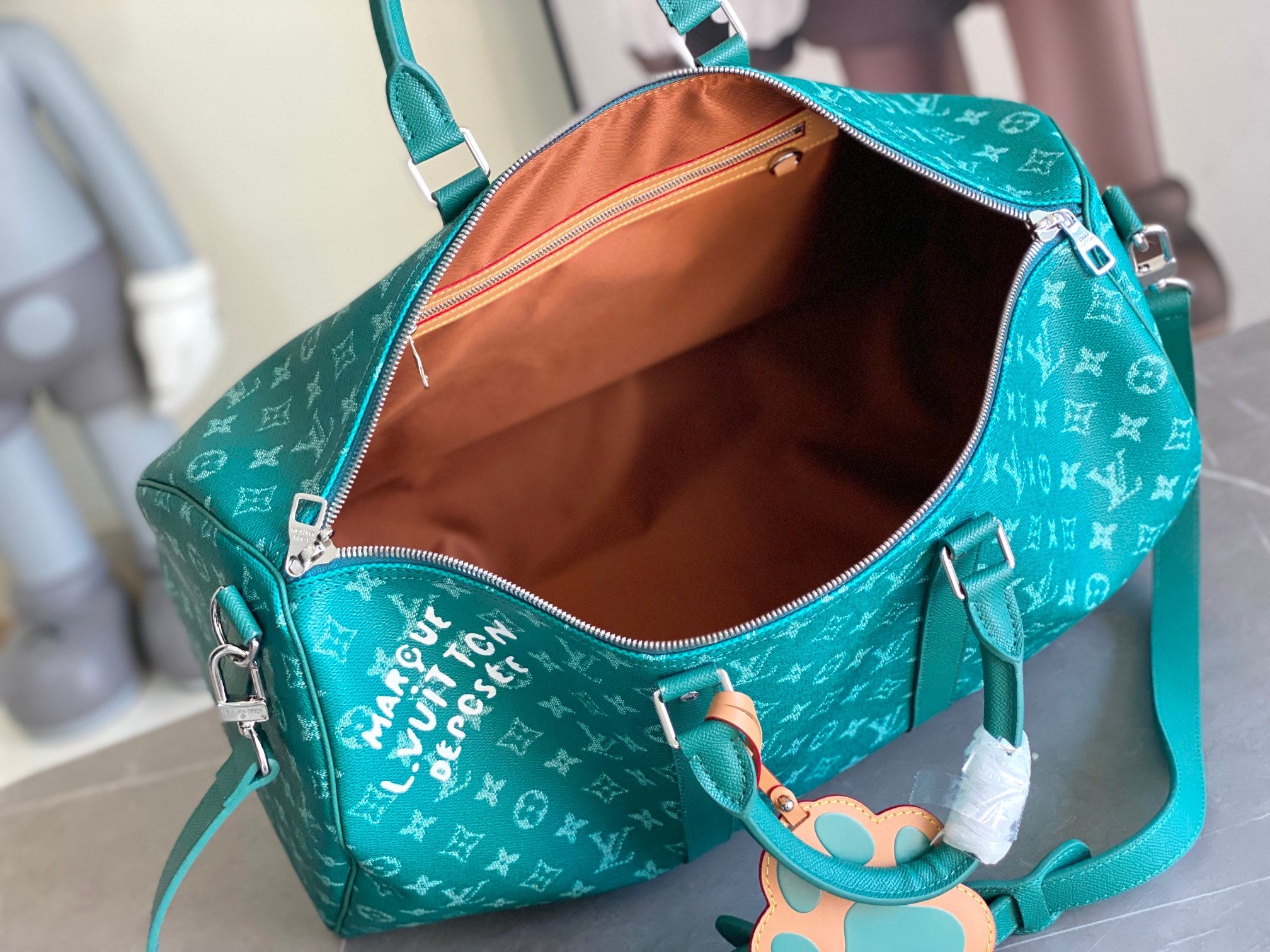 Teal monogram duffel bag open to warm tan interior with zip closure and side pocket