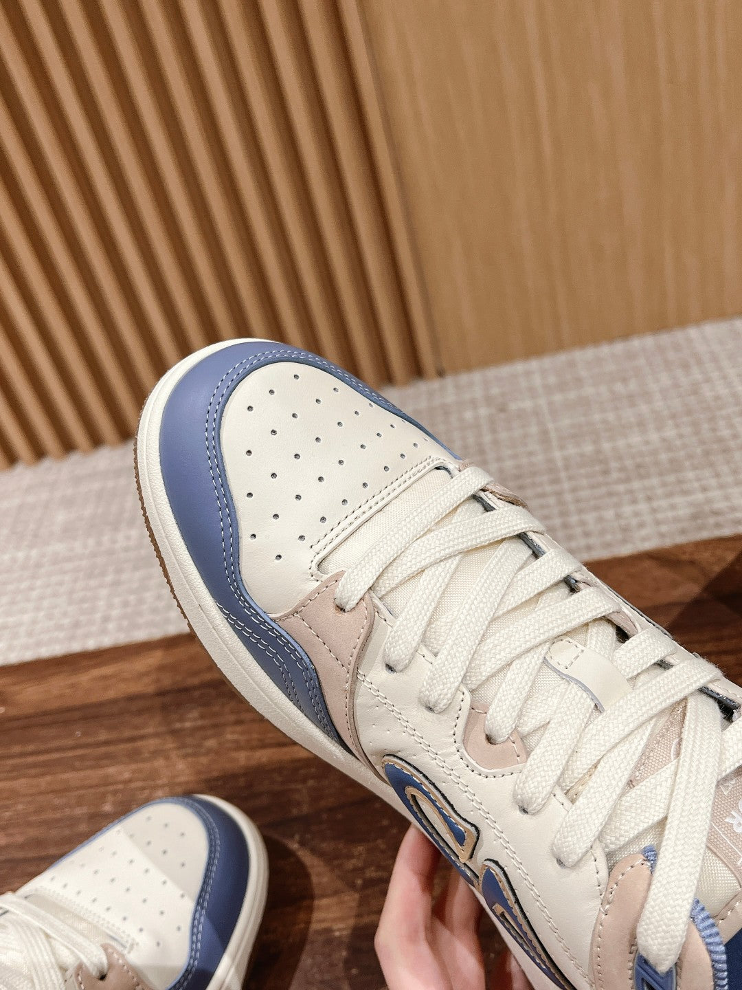 Dior unisex sneaker close-up, beige leather toe with perforations and blue collar.