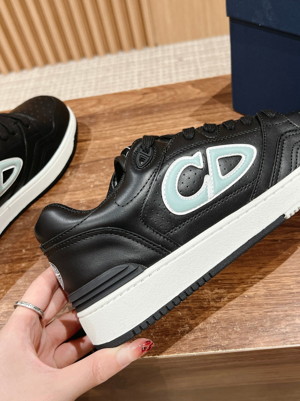 Black low-top sneaker close-up with light blue and white side logo, white sole