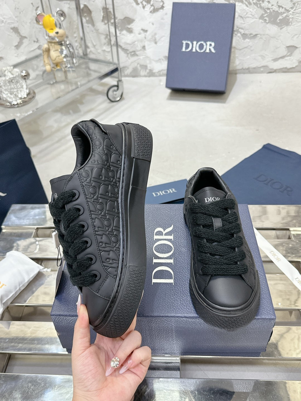 Black lace-up sneakers with textured side panel and Dior logo, held near box