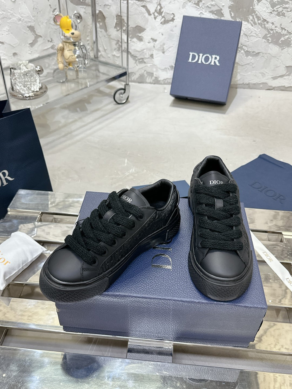 Black lace-up low-top sneakers with Dior logo branding, placed on box