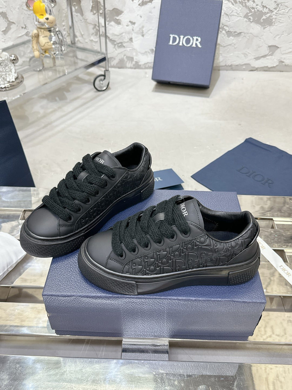 Black lace-up sneakers with embossed Dior monogram, shown on blue box