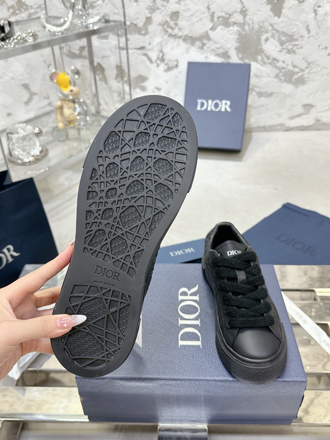 Black sneaker outsole with tread pattern, Dior logo on side near box