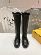 Black knee-high boots with side pull tabs and rounded toe, flat sole.