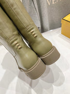 Olive green knee-high boots close-up with stitched panels and decorative eyelets.