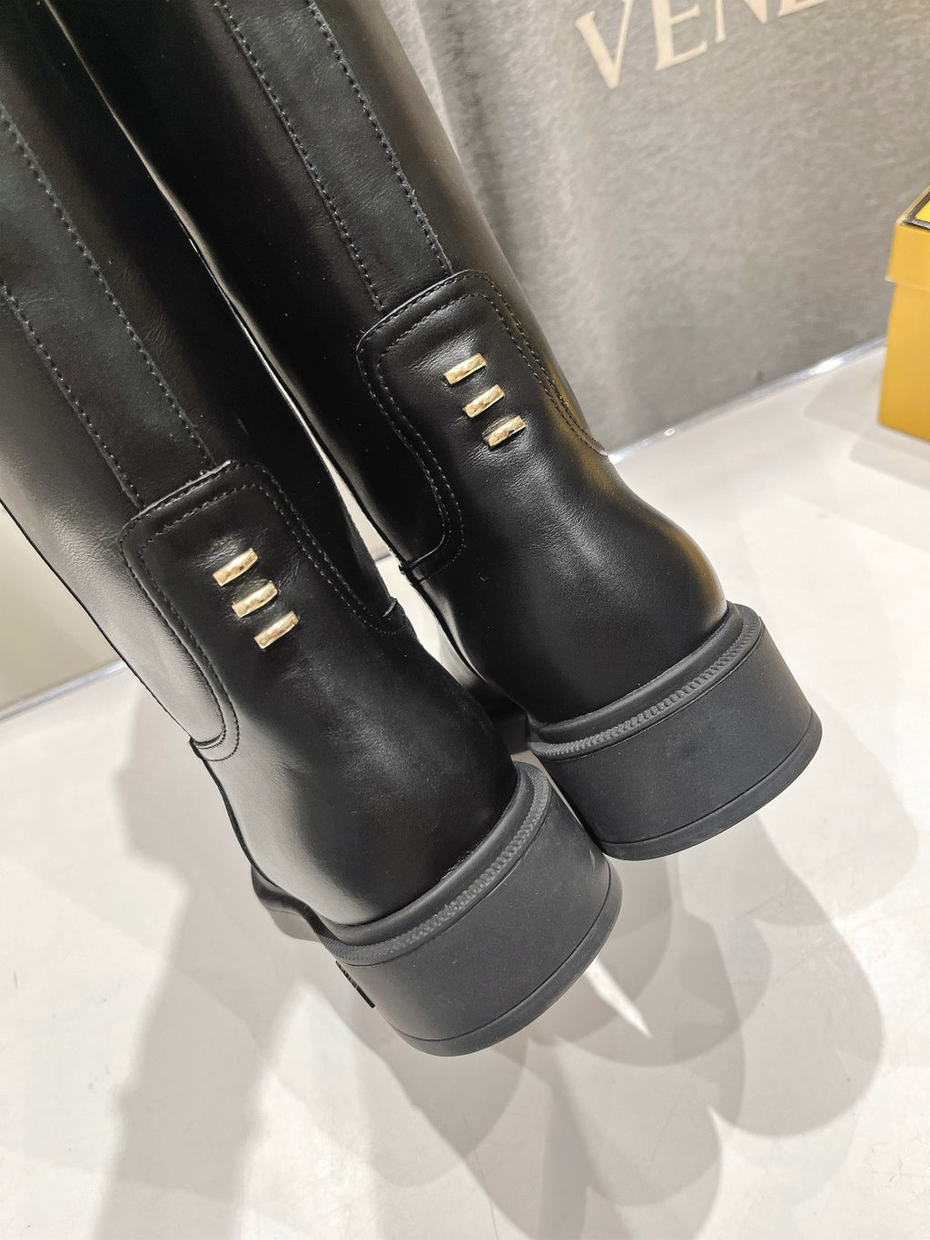 Black knee-high boots with cuff seam and gold logo detail near strap
