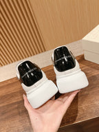 White low-top sneakers with glossy black heel branding, held in hand