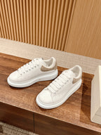 White sneakers with perforated toe and beige heel accents, placed on a shelf