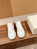 White lace-up sneakers with low-profile sole, shown on a wooden shelf