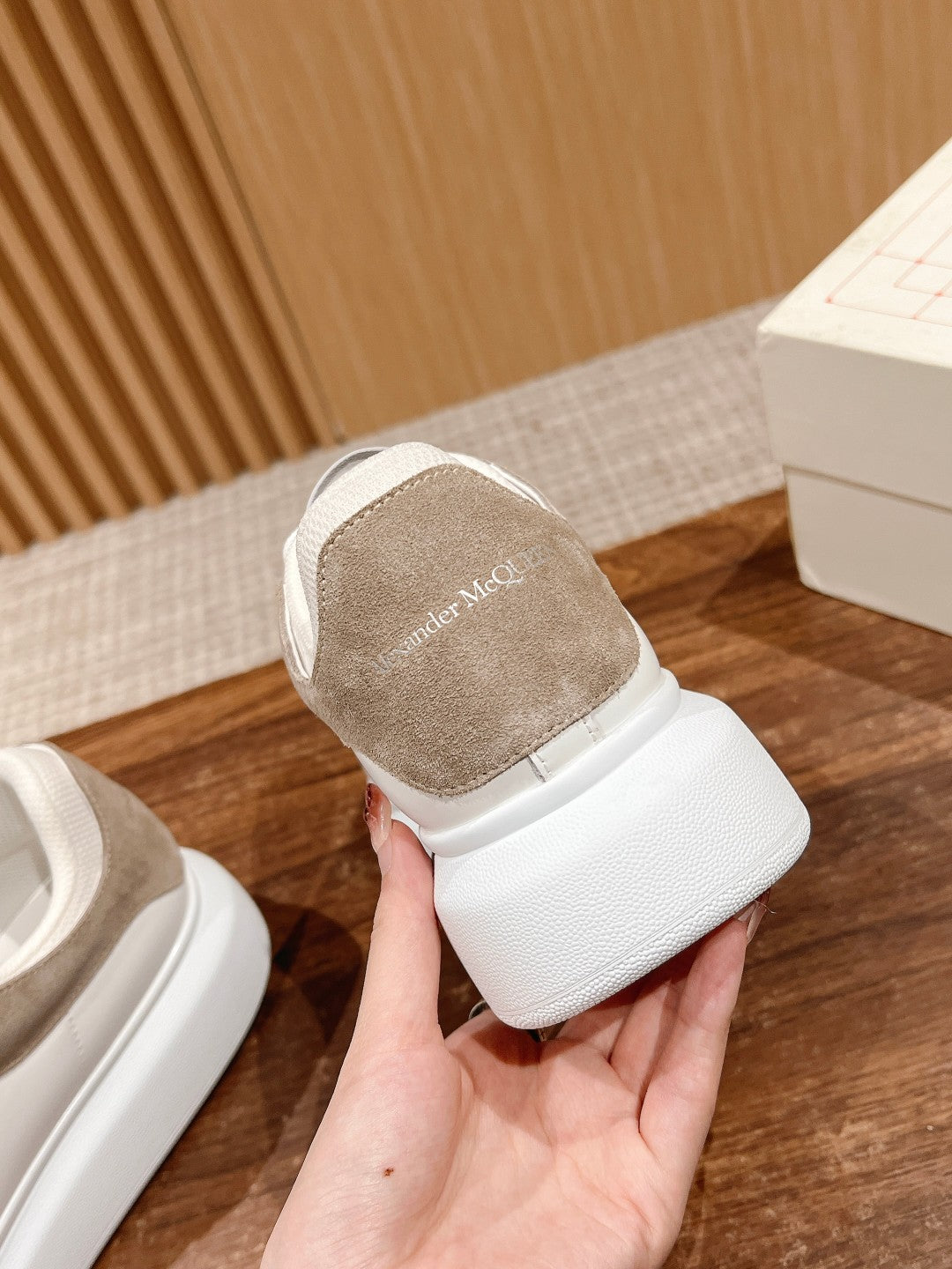 Heel view of white sneakers with beige suede collar and logo tab on back