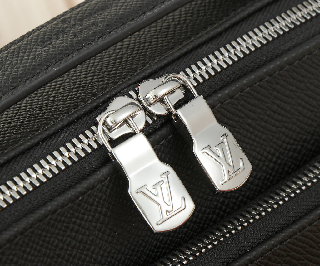 Close-up of black leather bag zipper with metal pulls and monogram logo plates.