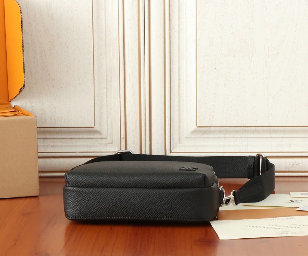 Black leather bag on tabletop, showing side profile and attached shoulder strap.