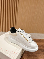 White low-top sneaker with black collar lining and gold eyelet accents
