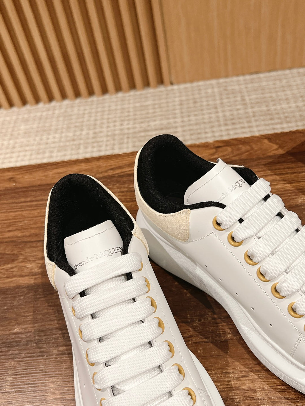 Two white lace-up sneakers with black lining and gold eyelet hardware
