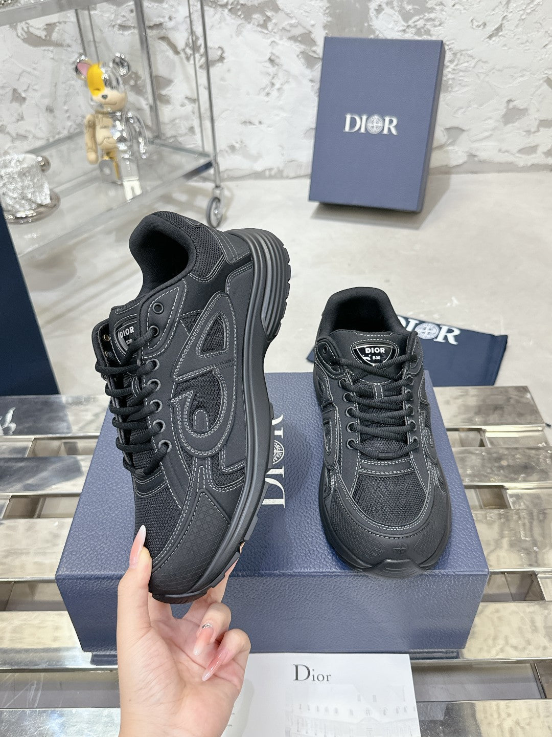 Charcoal gray lace-up sneakers, one held in hand over a blue display box