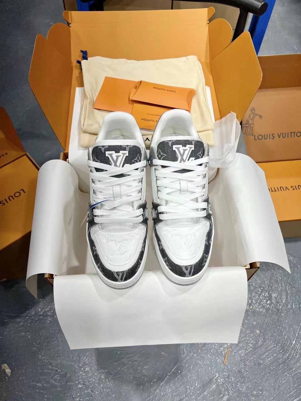 Pair of white Louis Vuitton trainer shoes with gray monogram side panels and white laces.