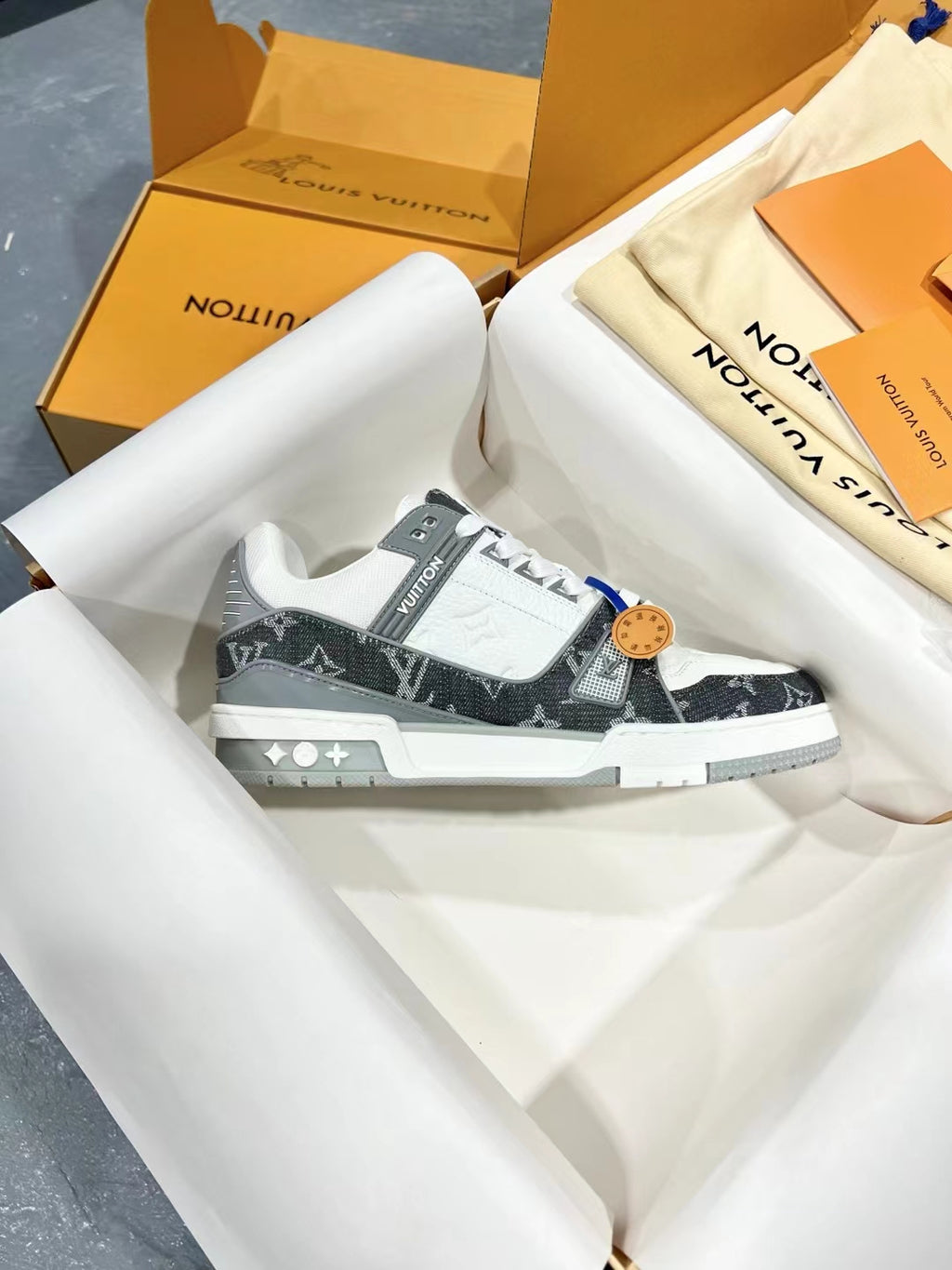 White and dark monogram Louis Vuitton trainer shoes on light paper, lace-up front.