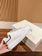 White lace-up sneakers with black trim, low-profile sole