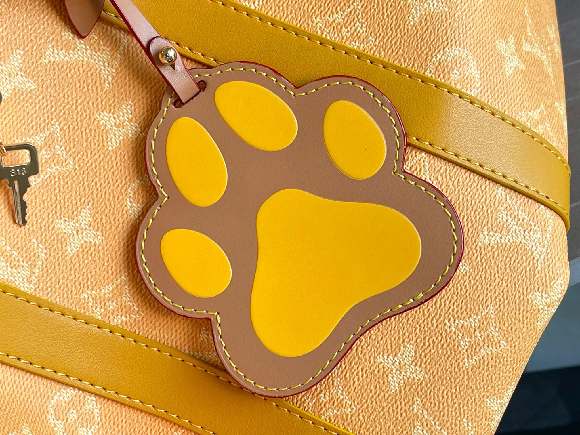 Yellow paw-shaped charm on Louis Vuitton monogram bag with stitched border