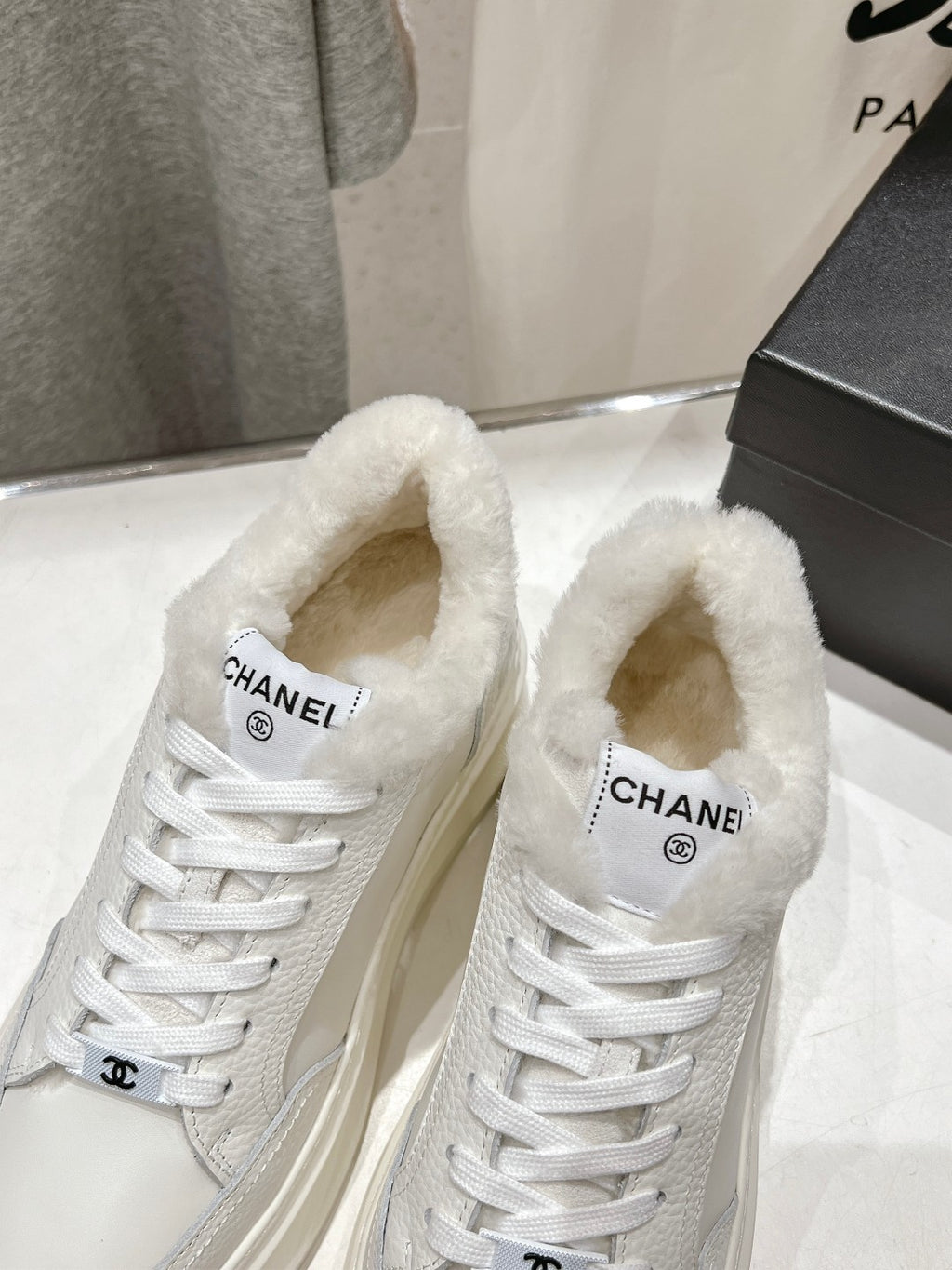 Close-up of white lace-up sneakers with faux-fur collar and Chanel logo on tongue