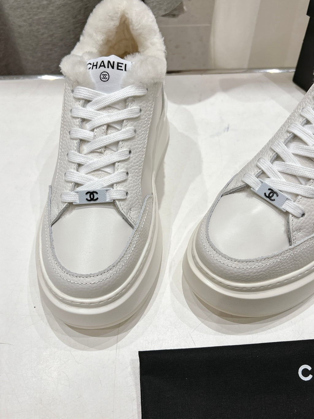 Side view of white lace-up sneakers with faux-fur collar and Chanel logo strap