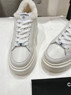 Side view of white lace-up sneakers with faux-fur collar and Chanel logo strap