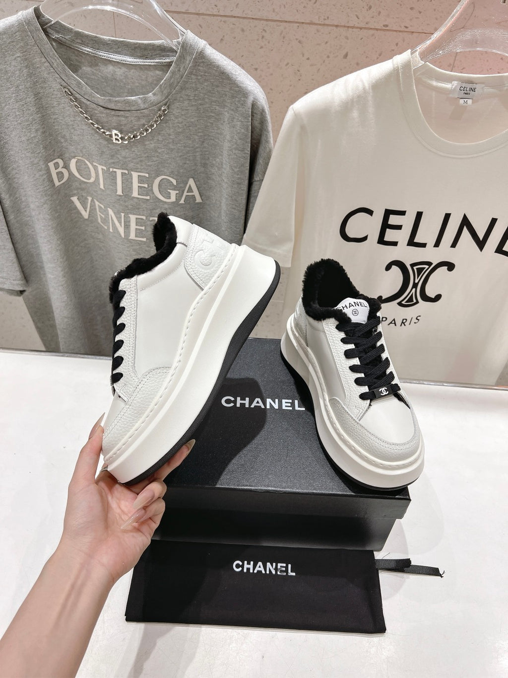White low-top sneakers with black faux-fur collar, black laces, and logo patch