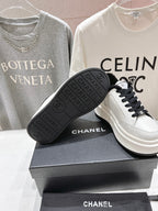 White sneaker with black outsole and Chanel branding, featuring black lace-up front