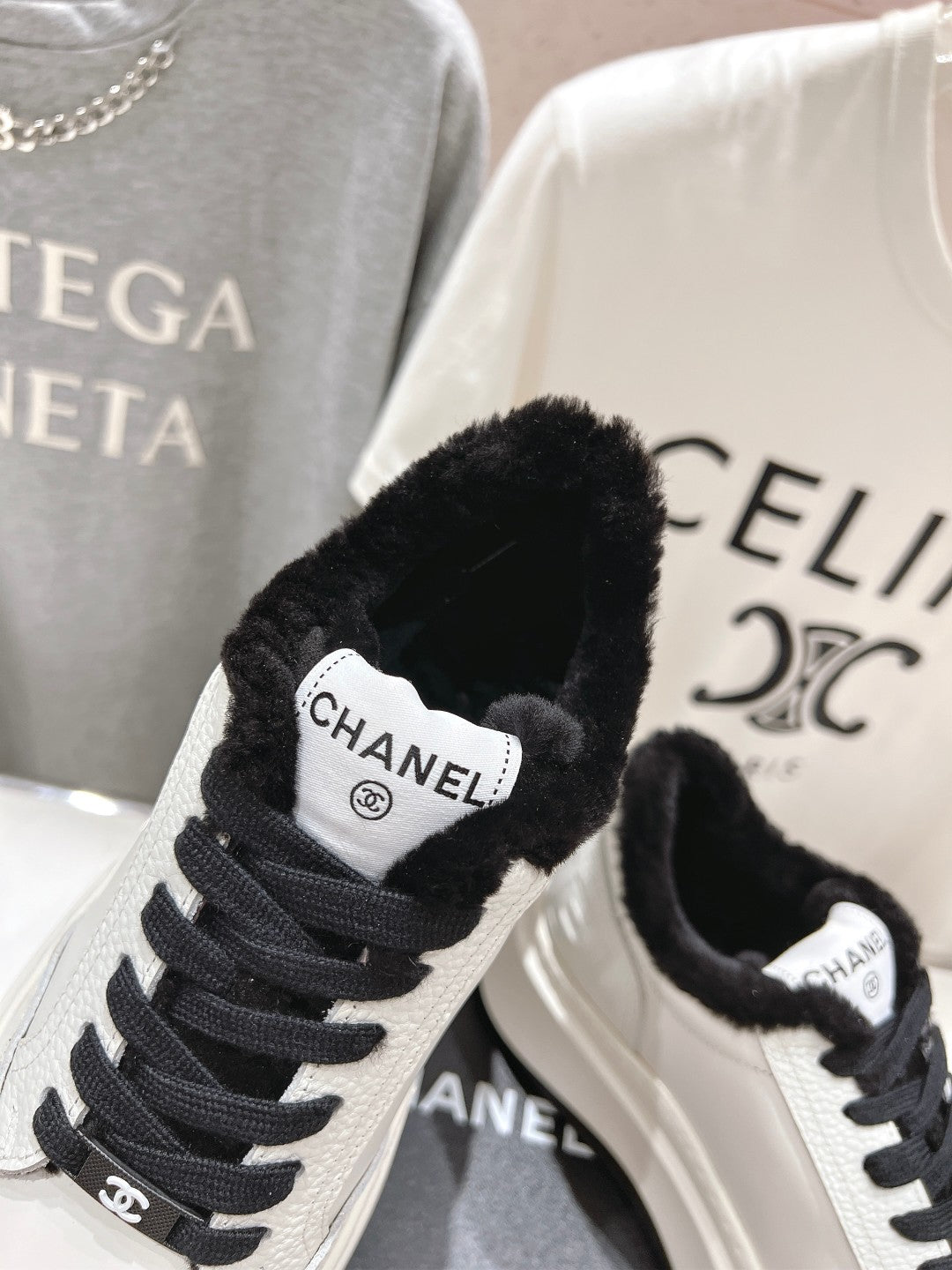 White sneaker close-up with black faux-fur collar, black laces, and Chanel patch