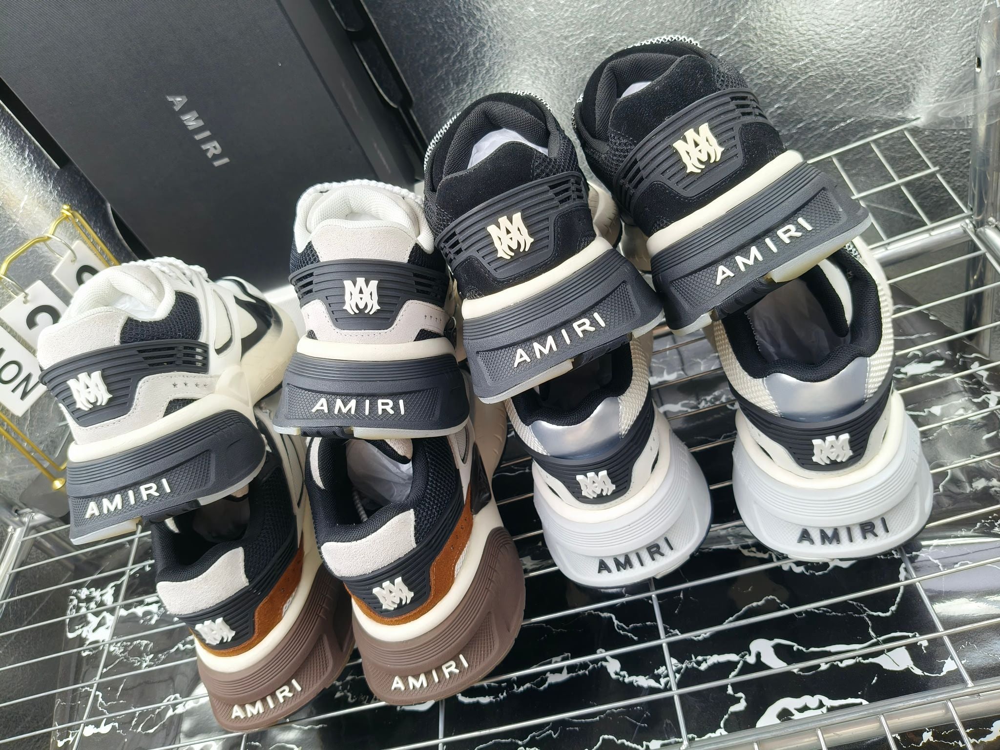 Amiri sneakers display: dark, white, and tan pairs on a metal rack