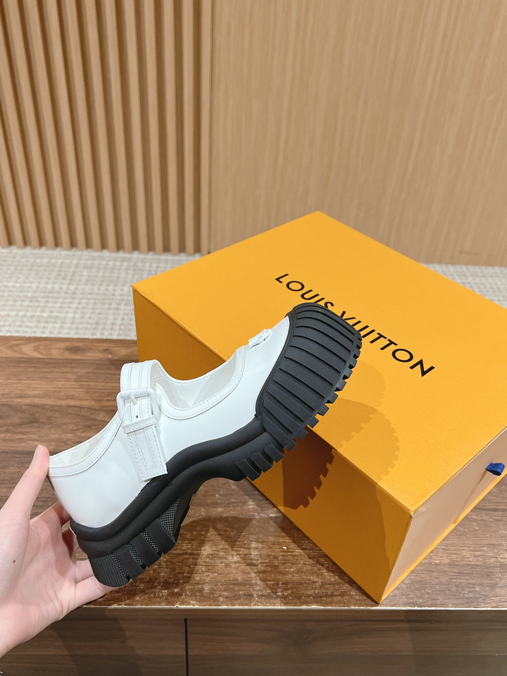 White sneakers with black lug outsole and Velcro strap, held in hand
