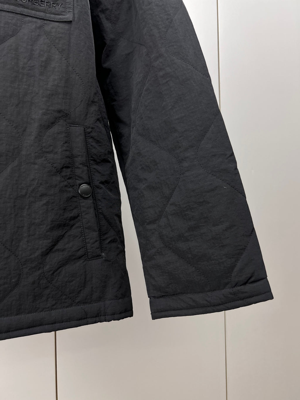 Quilted jacket sleeve and side seam, dark outer with buttoned cuff tab