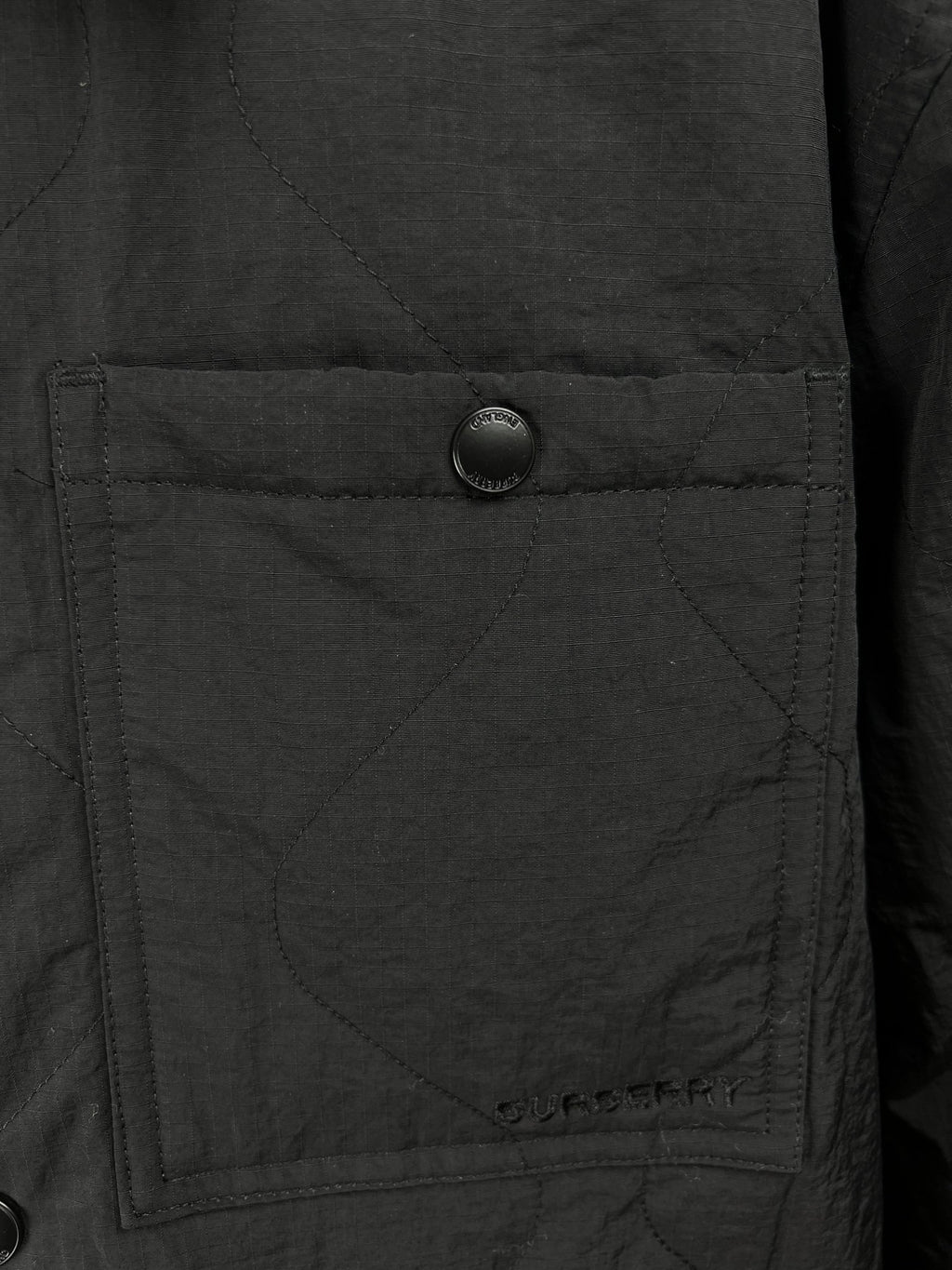 Quilted jacket pocket detail with round button on dark outer fabric