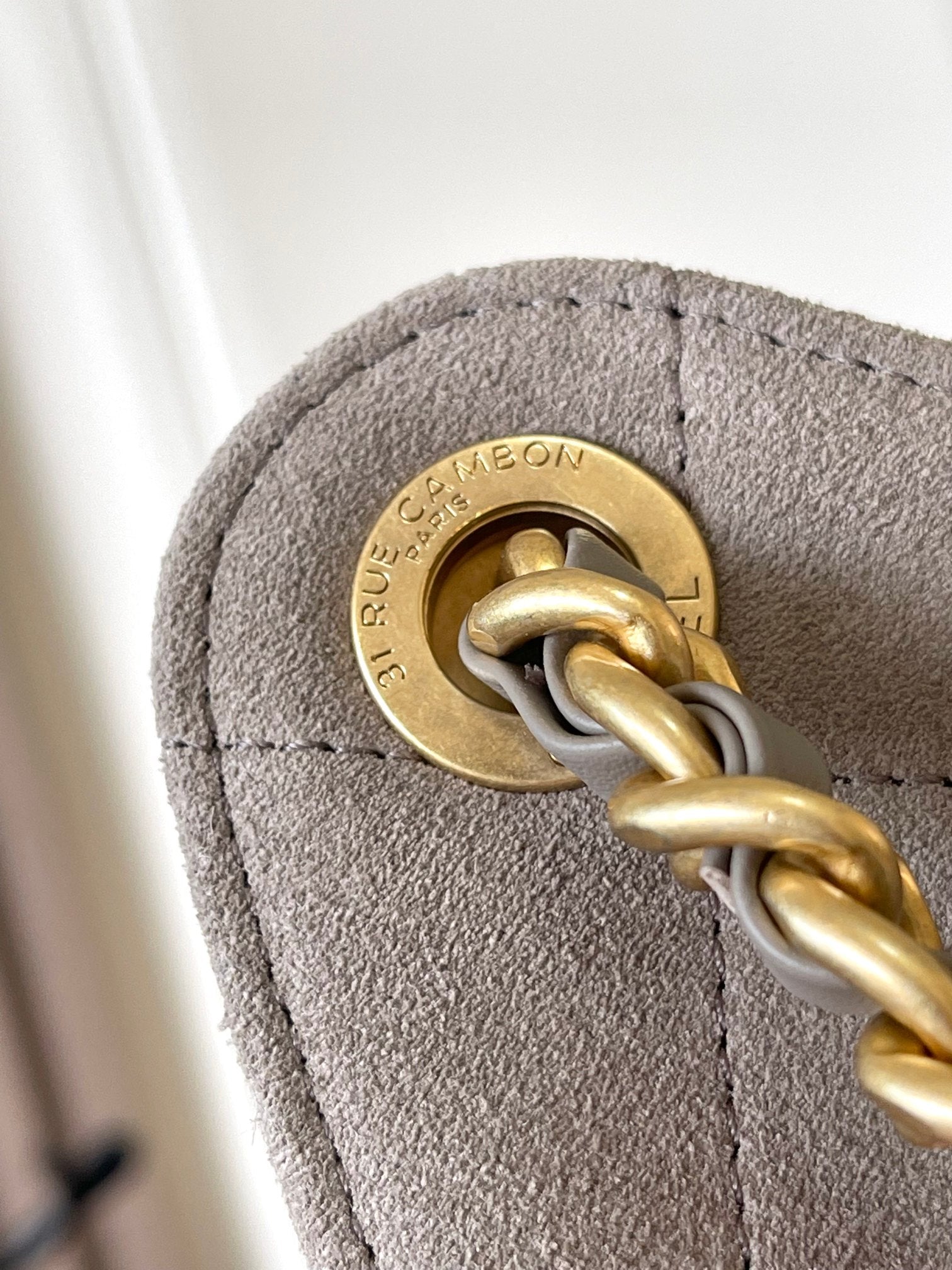 Gold-tone chain clasp hardware on gray suede-like fabric bag flap