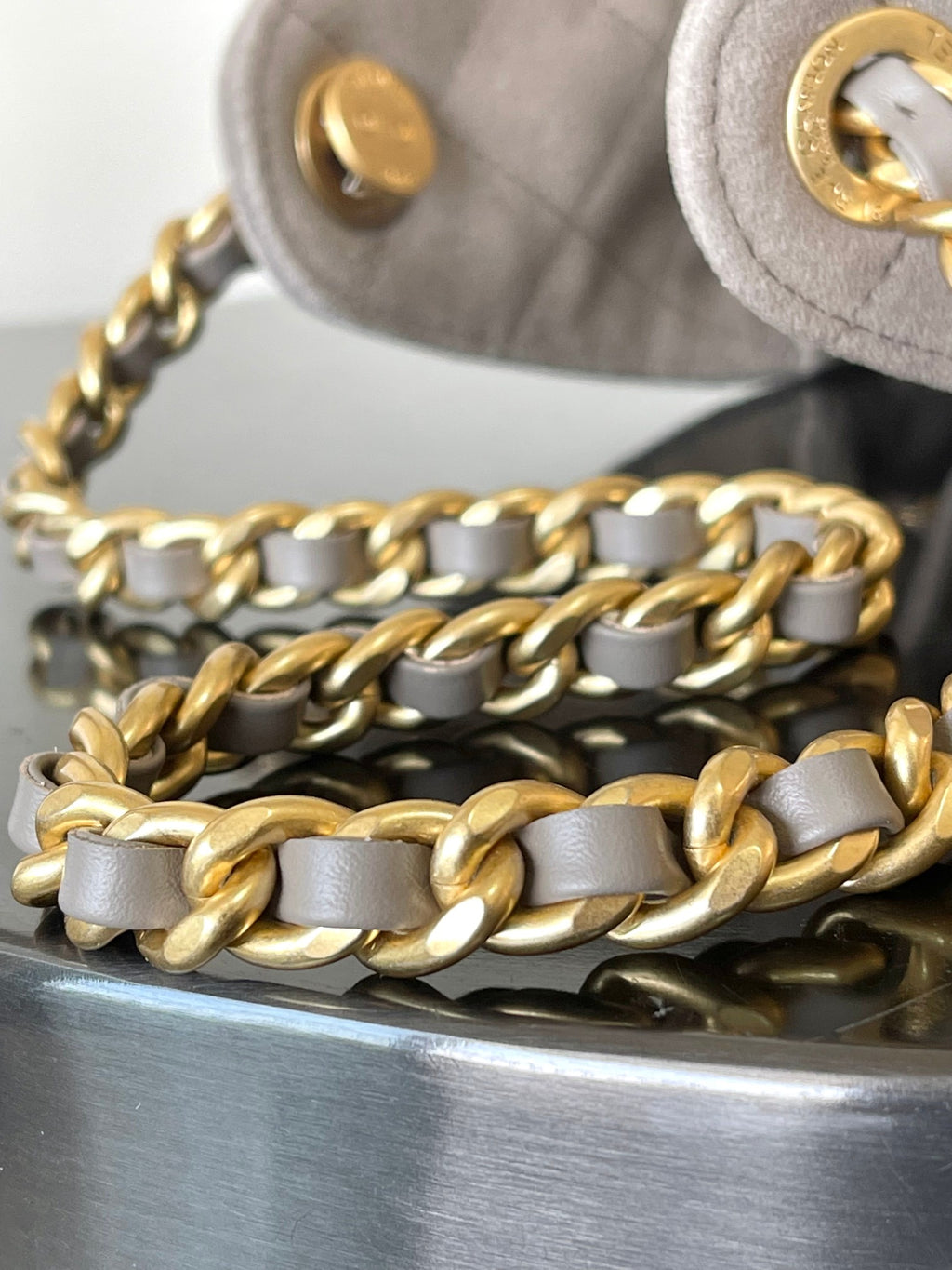 Gold-tone chain strap with light gray links and dark base on gray bag