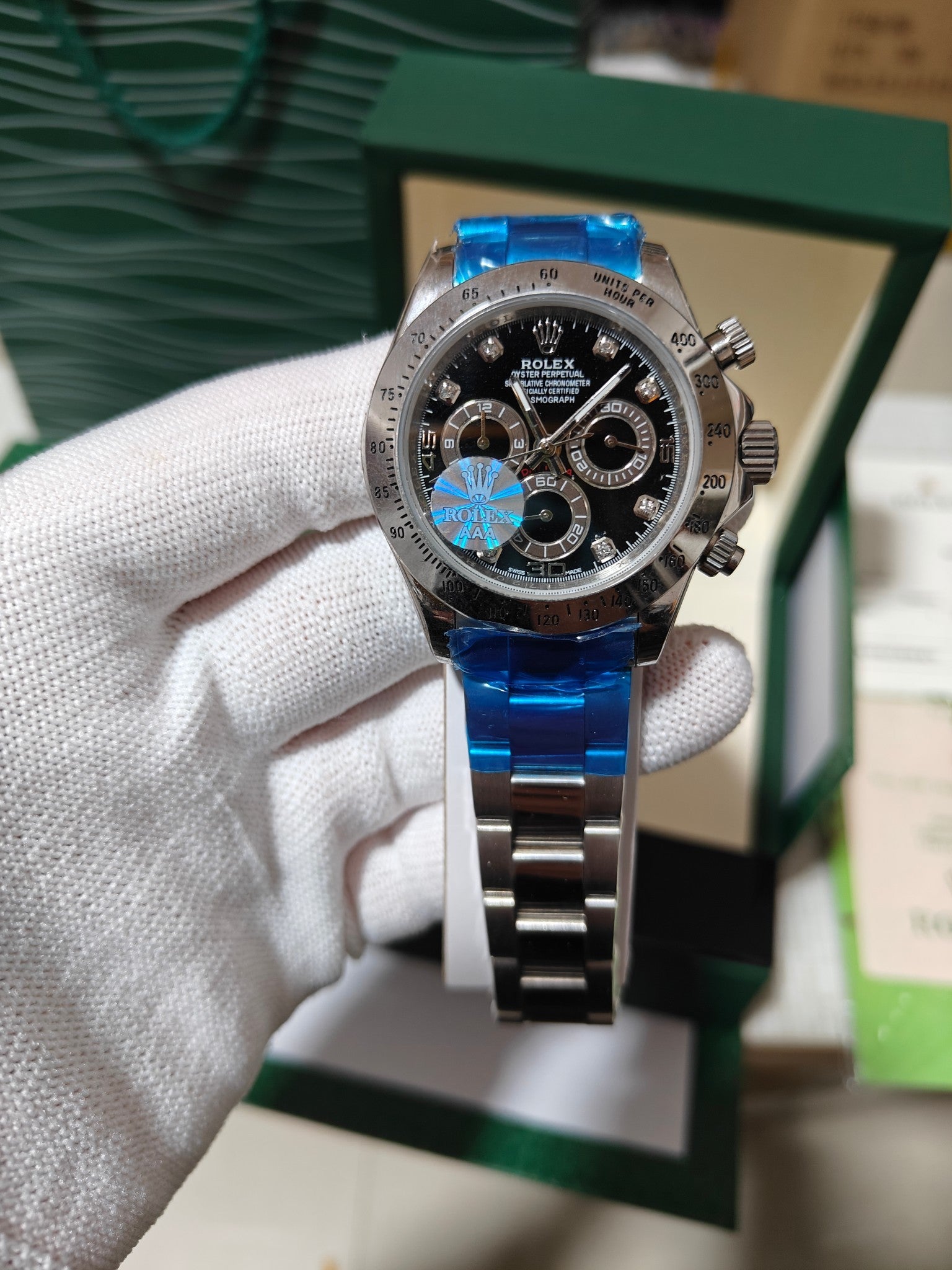 Rolex watch with black dial and metal link bracelet, blue reflection on glass.