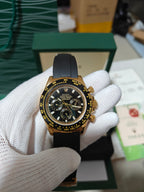 Rolex watch with dark dial, gold bezel and black rubber strap, multiple chronograph subdials.