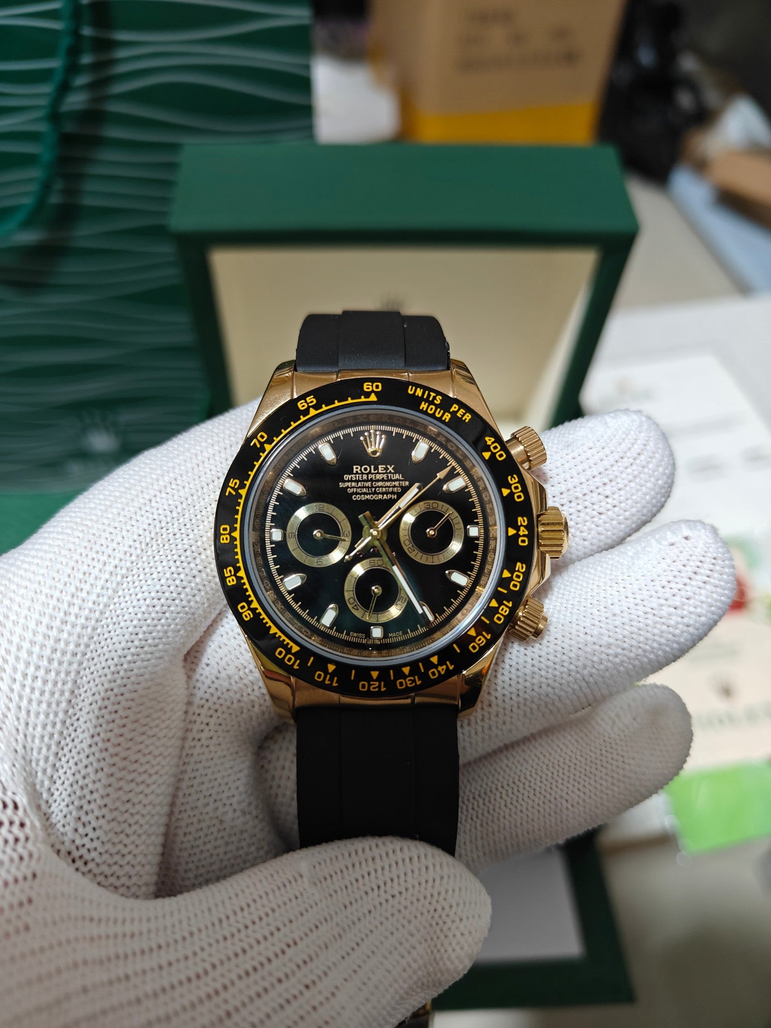 Rolex watch with dark dial and gold bezel, black rubber strap, close-up of chronograph subdials.