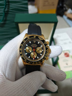 Rolex chronograph watch with black dial and red center seconds, gold bezel, black rubber strap