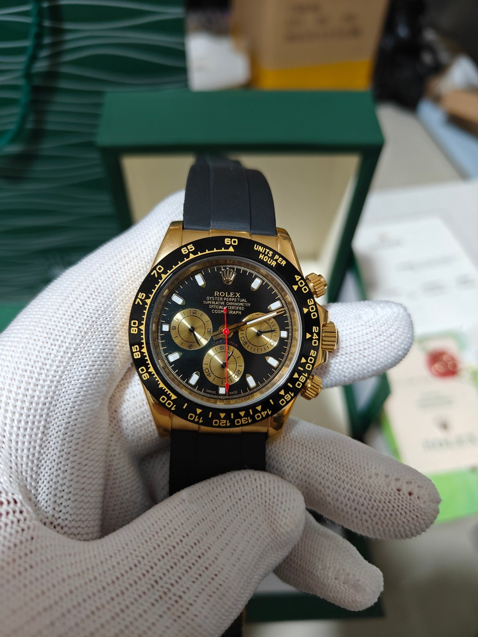 Rolex chronograph watch with black dial and red center seconds, gold bezel, black rubber strap