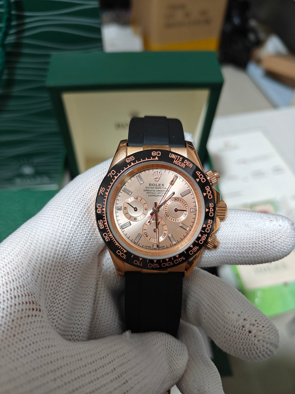 Rolex watch with light rose dial, gold bezel and black rubber strap, chronograph subdials.