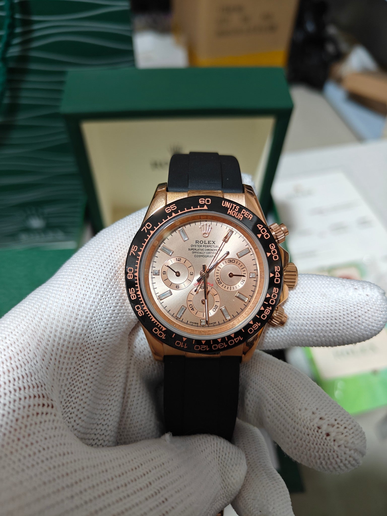 Rolex watch with light rose dial, gold bezel and black rubber strap, chronograph subdials.
