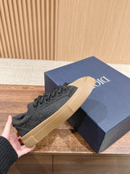 Black low-top sneakers with beige sole, laid on wooden surface next to blue box