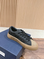 Black low-top sneakers with embossed pattern and beige rubber sole, on box