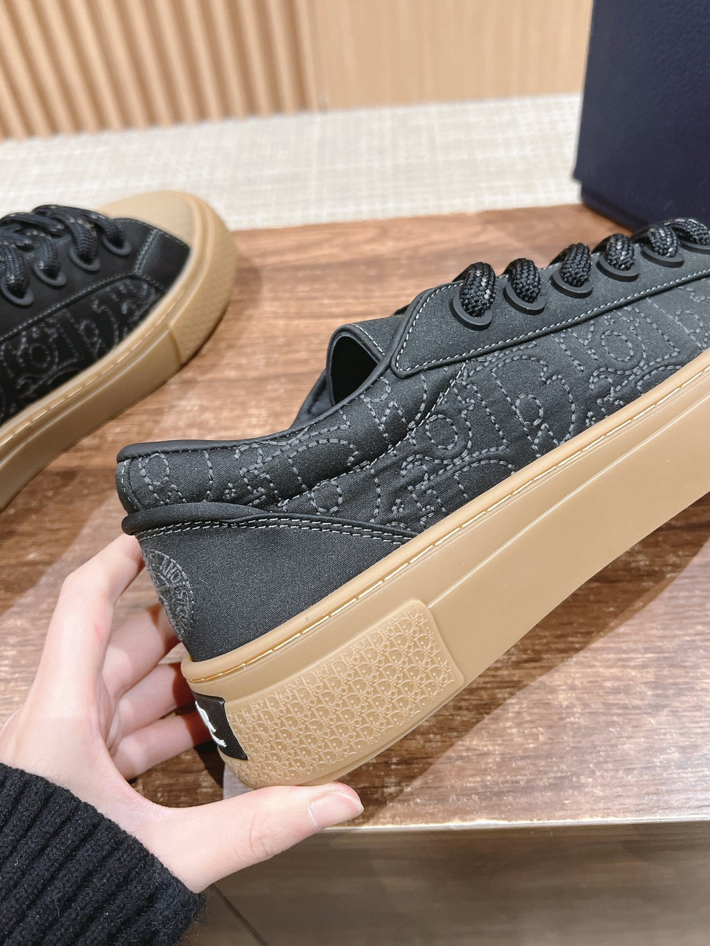 Black low-top sneakers held in hand, beige sole and lace-up front visible