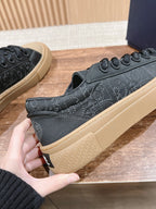 Black low-top sneakers held in hand, beige sole and lace-up front visible