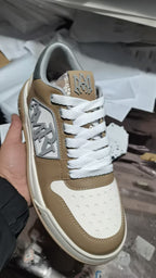 Tan and white sneakers with white laces and patterned side logo patch