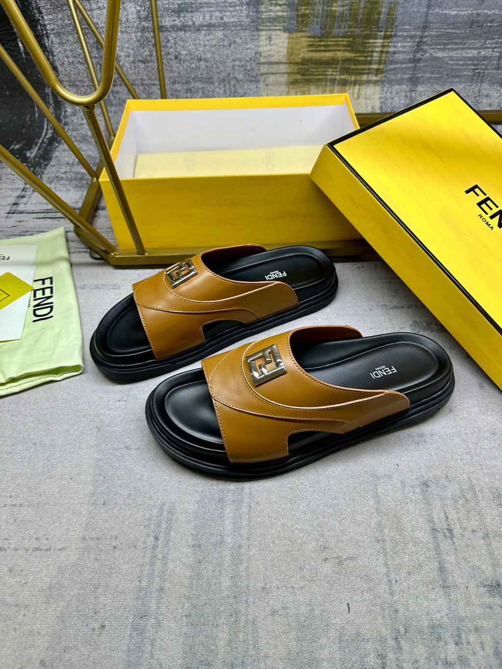 Fendi slide sandals with tan leather uppers, black soles, and gold logo buckle.