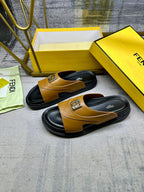 Fendi slide sandals with tan leather uppers, black soles, and gold logo buckle.