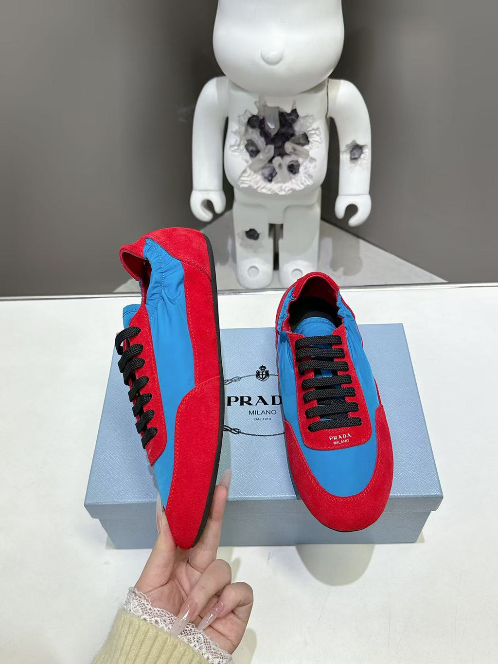 Prada unisex suede sneakers, red and blue with black laces, held for side view